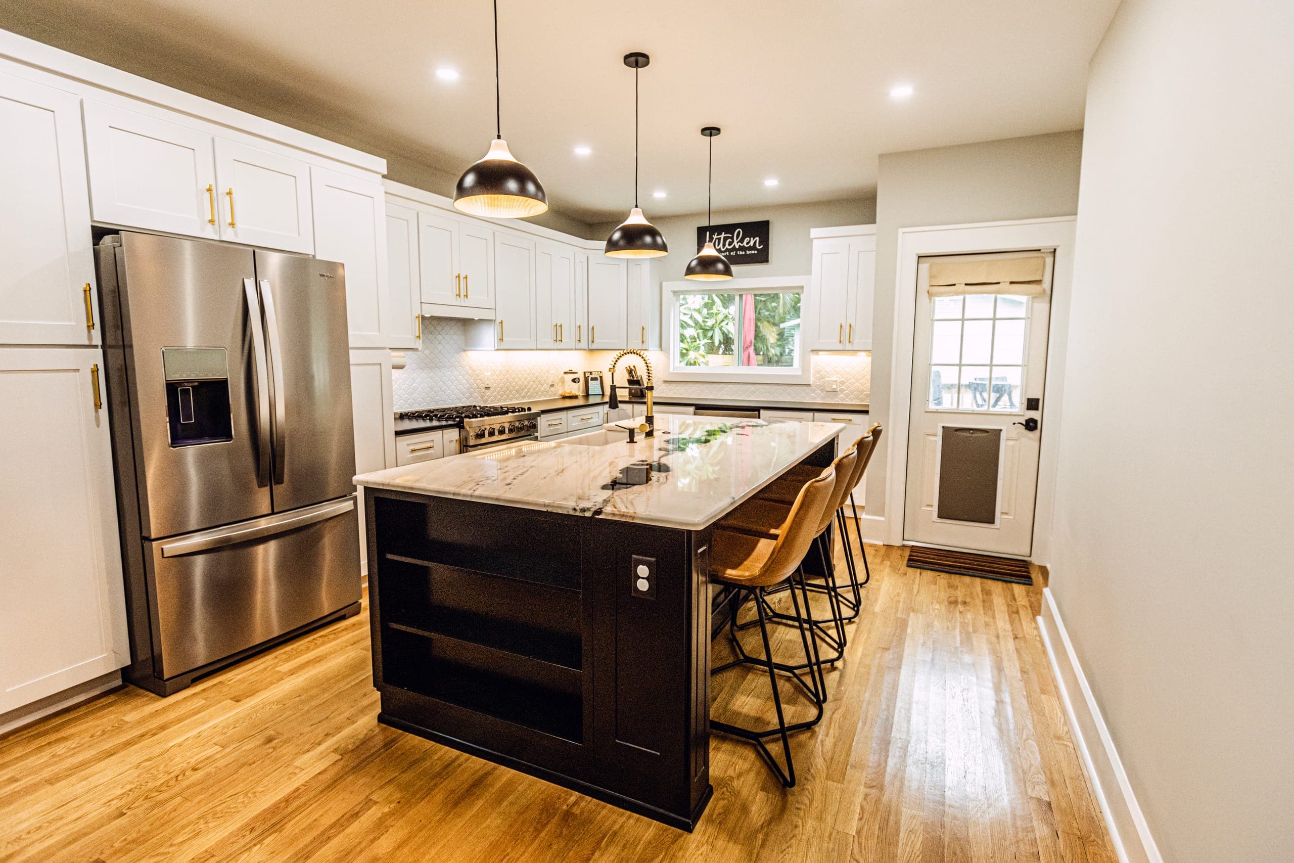 Open kitchen with white cabinets, black island, and pendant lights